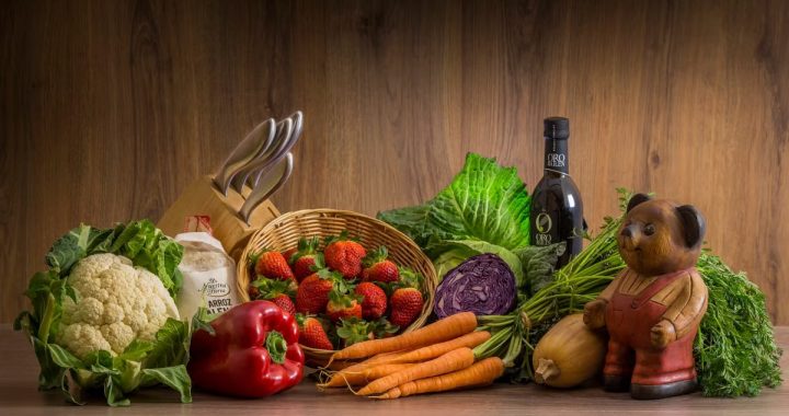 Arrangement of fresh vegetables and fruits on a wooden table with kitchen essentials.
