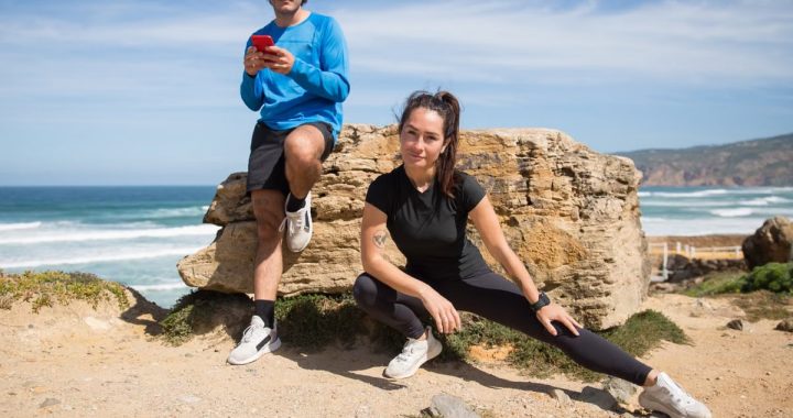 A couple stretching and using a phone on a scenic beach in Portugal.